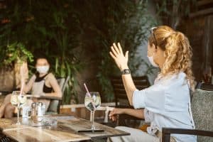 People Waiving Hi While Sitting Outside a Restaurant Wearing a Mask